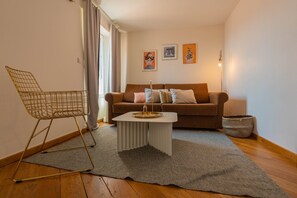 Ein Wohnzimmer mit einem braunen Sofa, einem weißen Couchtisch, einem goldfarbenen Stuhl aus Draht und einem grauen Teppich.