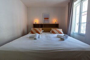 A hotel room with a bed, two bedside lamps, a framed picture on the wall, and a window with curtains. - Agréable et Cosy - Suquet - proche des plages (Cannes)