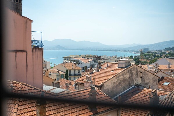 A coastal cityscape with terracotta-roofed buildings, a clear view of the sea, and distant mountains. - Agréable et Cosy - Suquet - proche des plages (Cannes)