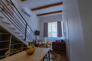 Un salon moderne avec un escalier, un téléviseur à  écran plat, un coin repas agrémenté d’un vase et un canapé.