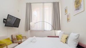 A hotel room with a bed, a desk, a chair, a TV, a window with curtains, and artwork on the walls. - Agréable et Cosy - Suquet - proche des plages (Cannes)