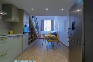 Une cuisine compacte dotée d’un four encastré, un coin repas avec une table et des chaises, et un escalier menant à un niveau supérieur.