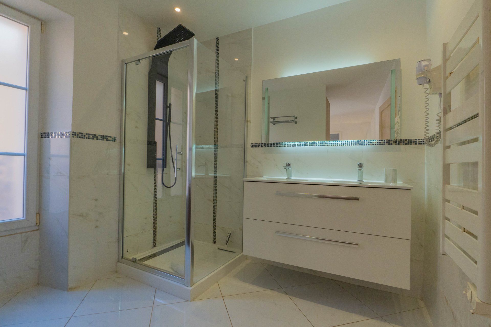 Un baño moderno con ducha de vidrio, tocador blanco con espejo y piso de baldosas.