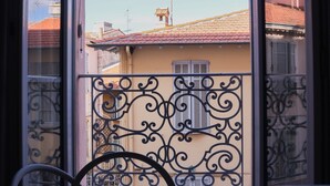 Ein Balkon mit aufwendig gestalteten Metallgeländern, einem Fahrrad und Blick auf benachbarte Gebäude mit roten Ziegeldächern.