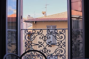 Een balkon met sierlijk metalen hekwerk, een fiets en uitzicht op omliggende gebouwen met rode dakpannen.