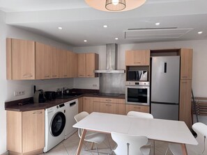 Eine moderne Küche mit Holzausstattung, einer Edelstahl-Dunstabzugshaube, einer eingebauten Mikrowelle, einem Kühlschrank und einer Waschmaschine.