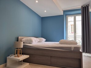 Ein Schlafzimmer mit einem Bett, einem Nachttisch mit Lampe und einem Fenster mit Vorhängen.