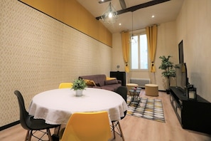 A modern living room with a round dining table, yellow chairs, a sofa, a TV, and a patterned wall.