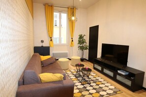 Un salon avec un canapé, un téléviseur et un tapis à motifs.
