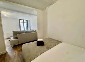 Ein schlicht eingerichteter Raum mit einem Bett, einer Couch und einem Fenster.