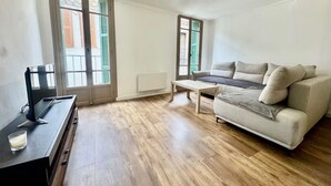 A room with a sofa, a coffee table, a TV on a stand, and a window with shutters.