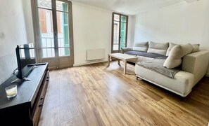 Ein Zimmer mit einer Couch, einem Couchtisch, einem Fernseher auf einem Schrank und einem Fenster mit Rollläden.
