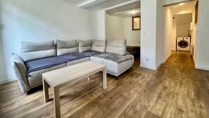 A modern living room with a sectional sofa, a wooden coffee table, and a laundry area visible through an open door.