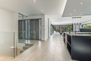 Eine moderne Küche mit einer großen Kochinsel, Glastüren, die auf einen Balkon führen, und einer Treppe.