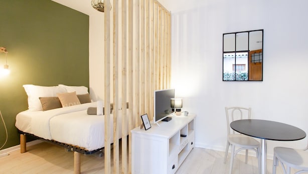 Een slaapkamer met een bed, nachtkastje, lamp, televisie en een eethoek met stoelen en een tafel.