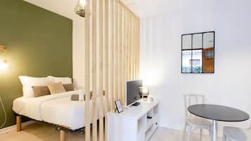 A bedroom with a bed, bedside table, lamp, TV, and a dining area with chairs and a table.