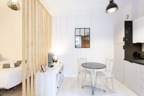 Ein stilvolles, minimalistisches Zimmer mit einem Bett, einem Schreibtisch mit Computer, einem runden Tisch mit Stühlen und einer Küchenzeile.