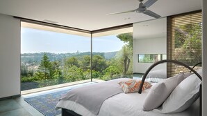 Una camera da letto moderna con un letto, una ventola a soffitto e vista su un paesaggio verde.
