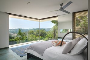 Ein modernes Schlafzimmer mit einem Bett, einem Deckenventilator und Blick auf eine grüne Landschaft.