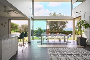 Una cuina moderna amb una illa gran, una zona de menjador amb taula i cadires de vidre, i vista a l'exterior.