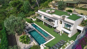 Una moderna casa a due piani con piscina, area salotto esterna e un muro in pietra.