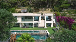 Una moderna casa a due piani con piscina, immersa nel verde e circondata da un muro in pietra.