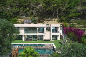 Ein modernes, zweistöckiges Haus mit Swimmingpool, umgeben von üppigem Grün und einer Steinmauer.