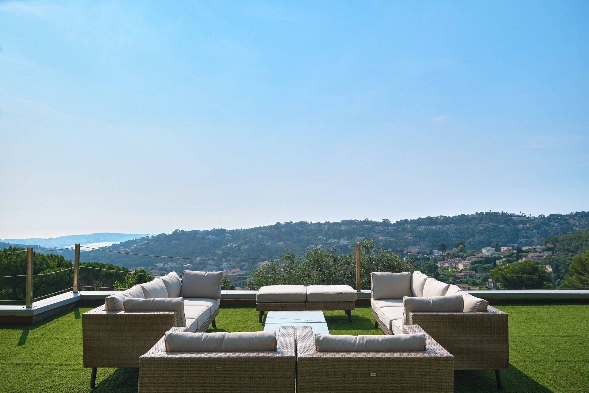 A rooftop terrace with wicker furniture and a view of a hilly landscape.
