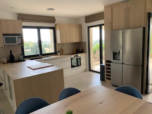 A modern kitchen with a central island, built-in appliances, and a sliding glass door to a balcony. - Superbe villa et piscine - 3 appartements (Cagnes-sur-Mer)
