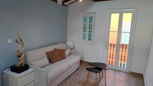 A living room with a sofa, a small table, a nightstand, a decorative sculpture, and a balcony with a railing. - Charmant studio rénové – Place de la République (Villefranche-sur-Mer)
