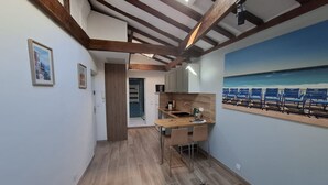 A narrow hallway with a wooden floor, a kitchen area with a sink and cabinets, and a painting of a beach scene on the wall. - Charmant studio rénové – Place de la République (Villefranche-sur-Mer)