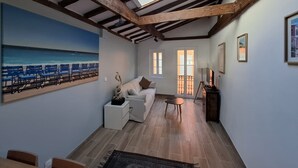 A room with a skylight, a painting of a beach, a sofa, a small table, and a TV. - Charmant studio rénové – Place de la République (Villefranche-sur-Mer)