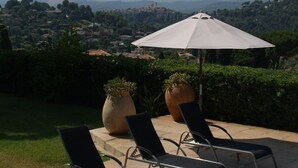 A poolside area with lounge chairs and an umbrella, overlooking a scenic landscape with hills and buildings. - Authentic & Atypical house - Vence (Vence)