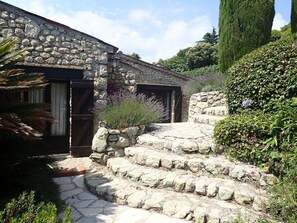 A stone building with a rustic entrance, steps leading up to a door, and a garden with various plants. - Authentic & Atypical house - Vence (Vence)