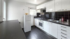 Ett modernt kök med vita skåp, en svart kakelbeklädd vägg bakom arbetsbänken, en inbyggd mikrovågsugn och en diskho i rostfritt stål.