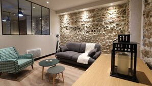 A living room with a stone wall, a sofa, a patterned armchair, two small tables, and a black lantern. - Superbe Appartement moderne au coeur du Vieux Nice (Nice)