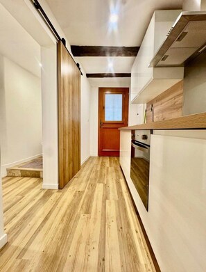 Ein schmaler Korridor mit Holzdielen, einer Holztür und einer weißen Wand.