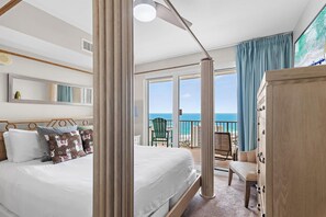 Ein Schlafzimmer mit Bett, Nachttisch, Kommode, Stuhl und einem Balkon mit Meerblick.