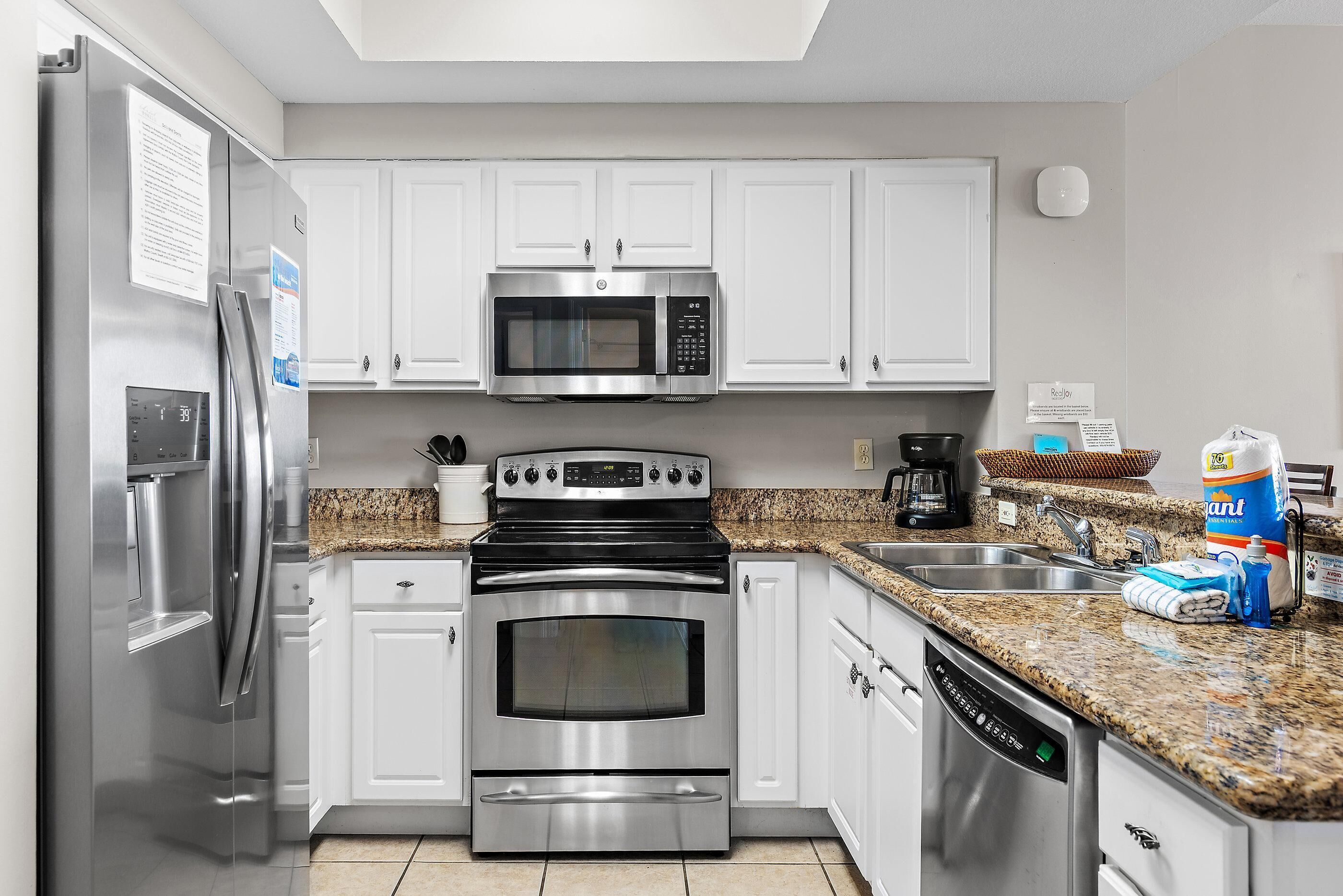 A kitchen with stainless steel appliances, white cabinets, granite countertops, and a dishwasher.