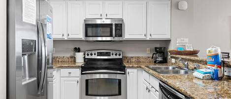 A kitchen with stainless steel appliances, white cabinets, granite countertops, and a dishwasher.