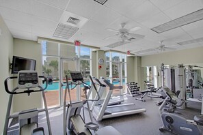 Ein Fitnessstudio mit Laufbändern, Crosstrainern und Kurzhanteln, großen Fenstern und einem Notausgang.