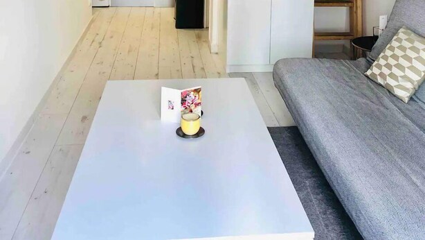 Un ambiente compatto con divano, tavolino, angolo cottura e soppalco adibito a camera da letto.