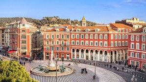 Una piazza storica con una fontana al centro, circondata da edifici rossi con finestre ad arco e balconi.