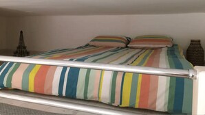 Un letto con copripiumino a righe e cuscini, una testiera in metallo, una piccola Torre Eiffel decorativa e un vaso con una superficie strutturata sul comodino.