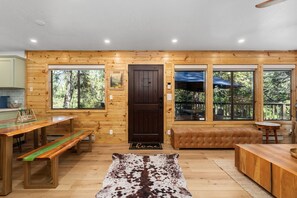 Ein Holzblockbau-Innenraum mit Esstisch, Bänken, einer Couch und einem Teppich.