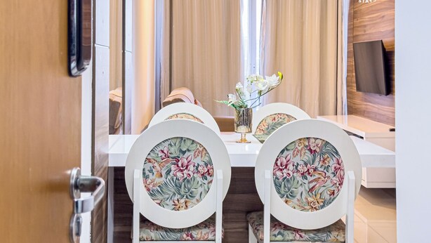 Un comedor con mesa blanca, sillas con motivos florales, un jarrón con flores y una lámpara colgante.