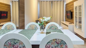 Un comedor con una mesa blanca, sillas estampadas, un jarrón con flores y un cartel de Netflix en la pared.