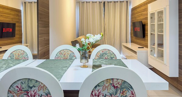 A dining area with a white table, floral chairs, a vase with flowers, and a Netflix sign on the wall.