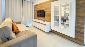 Una sala de estar moderna con un sofá gris, un mueble de entretenimiento blanco y una vitrina de vidrio con objetos decorativos.