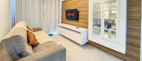 Un soggiorno moderno con un divano grigio, un mobile TV bianco e una vetrina contenente oggetti decorativi.